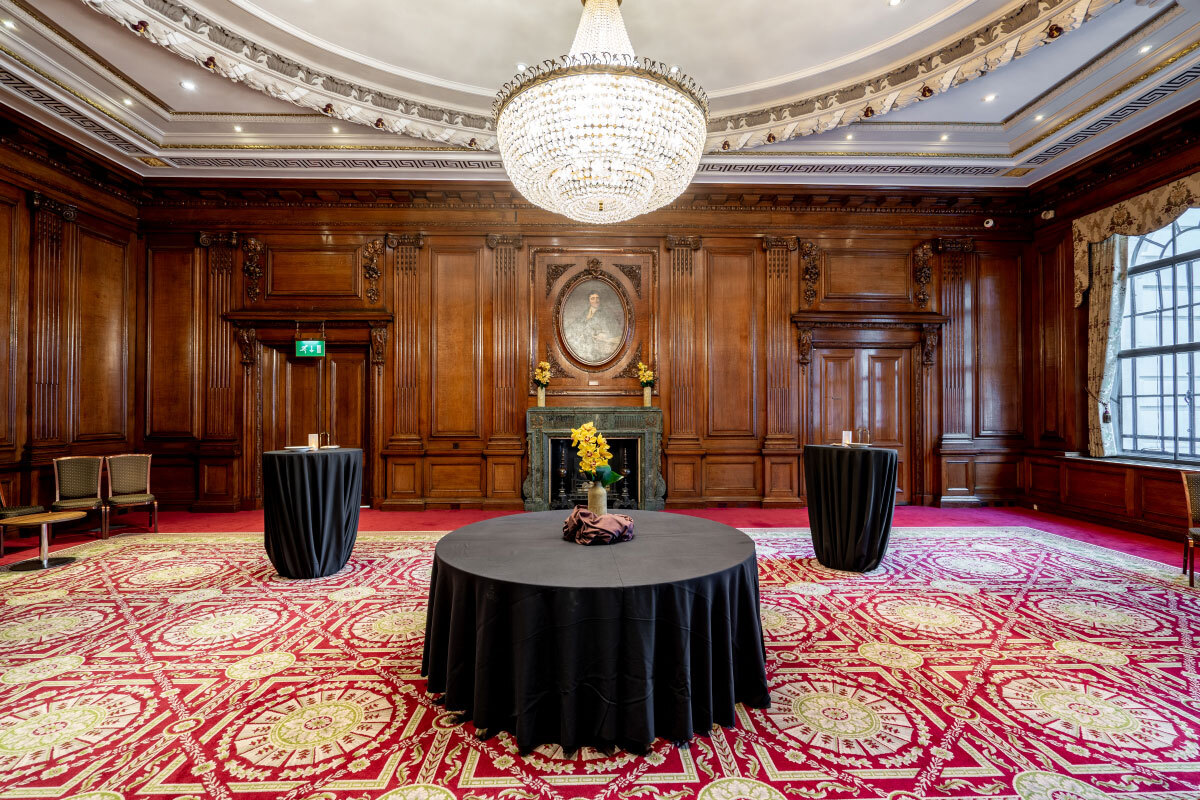 A wood-panelled room inside One Great George Street, with a crystal chandelier and a red patterned carpet